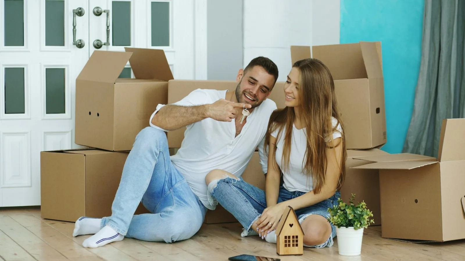 Jeune couple assis parmi les cartons de déménagement dans son nouveau logement, une clé à la main